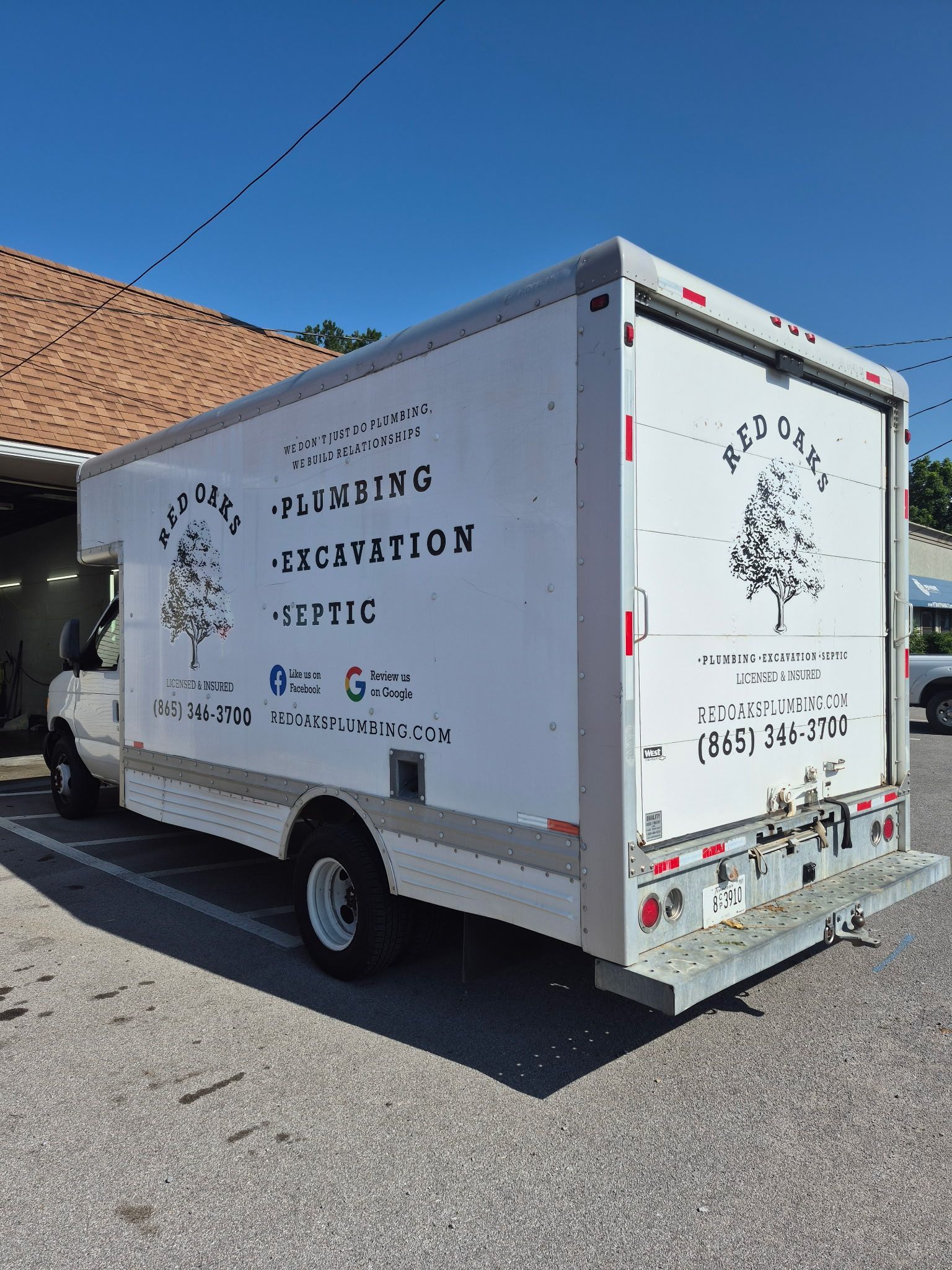 White plumbing/septic service truck parked beside a building under a blue sky.