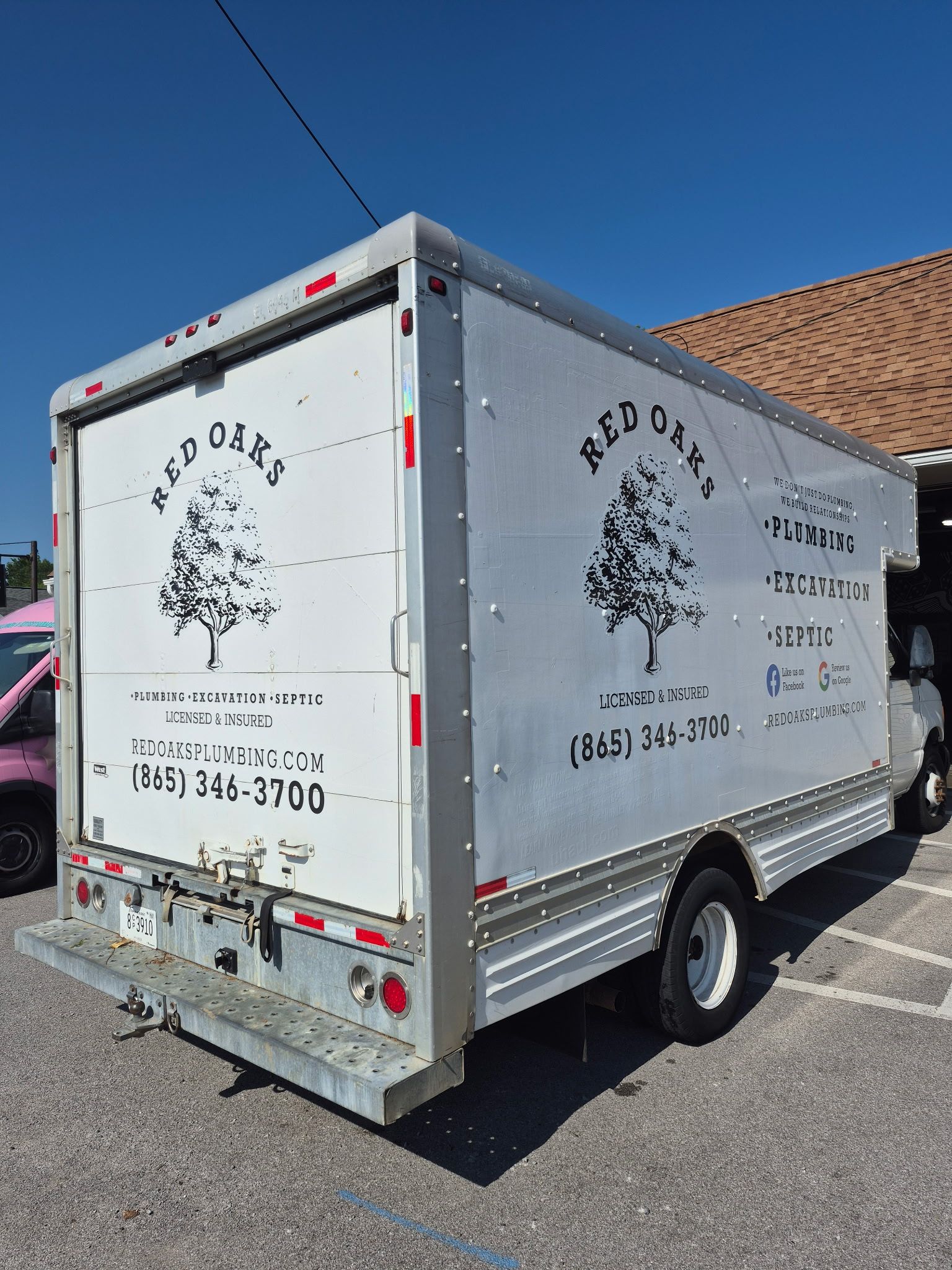 White box truck with tree logo parked on a sunny street beside a building under a blue sky.