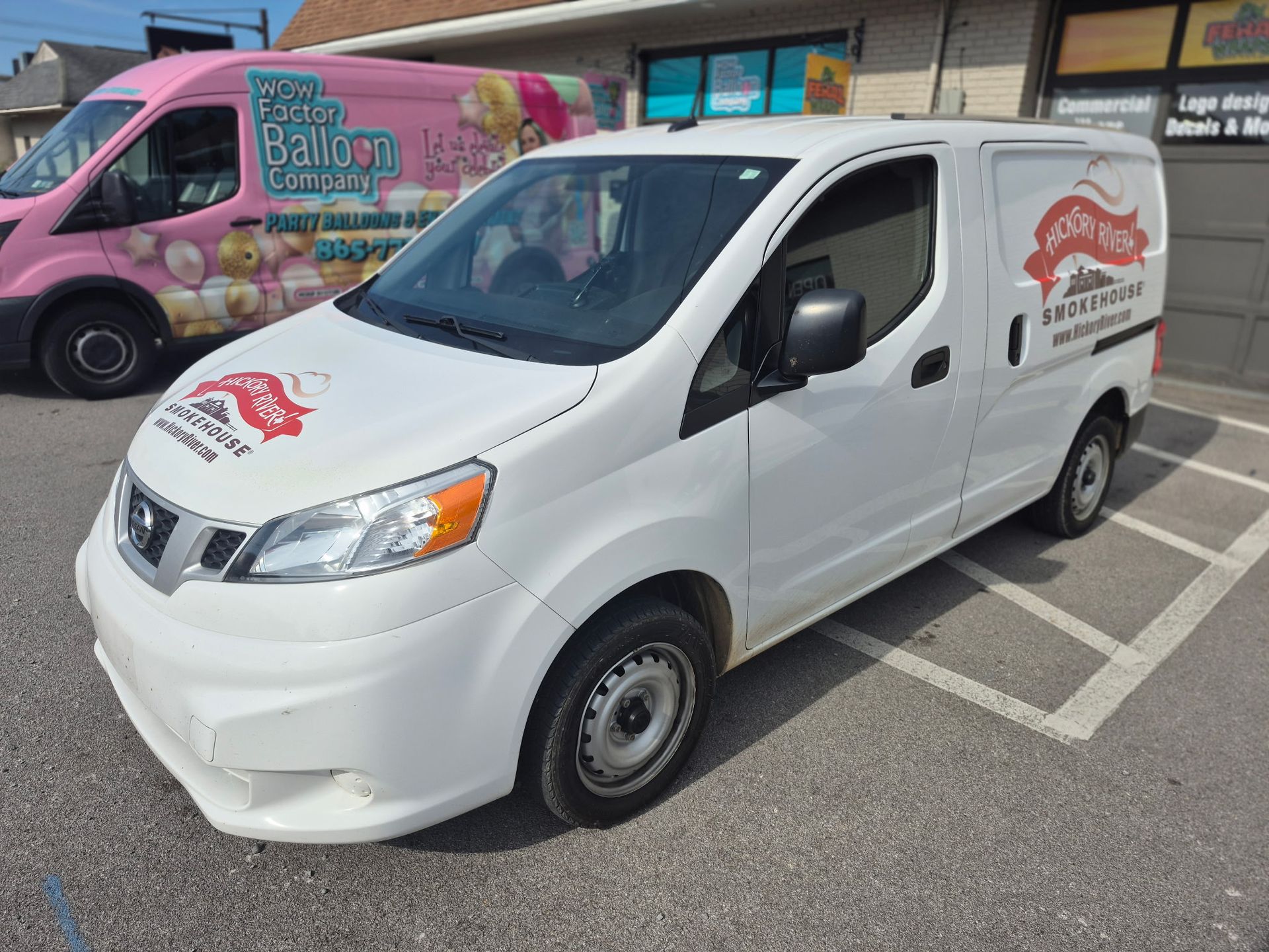 White delivery van with red logo parked in a lot beside a colorful food truck