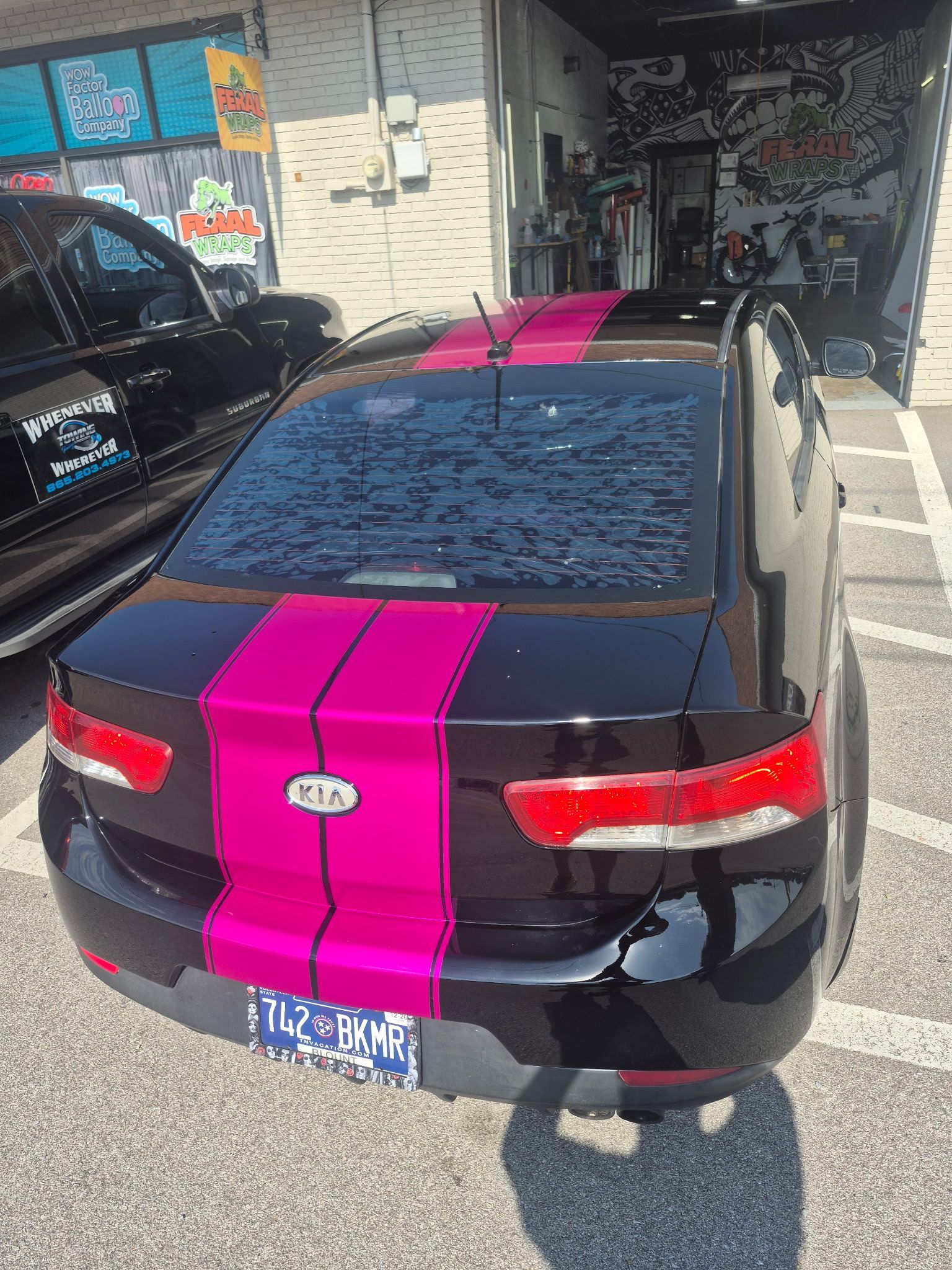 Black sedan with bright pink racing stripes parked beside a storefront