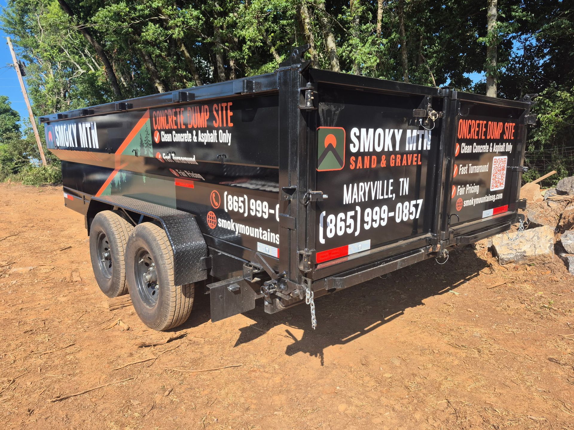 Black dump trailer with Smoky services branding parked on dirt road near trees