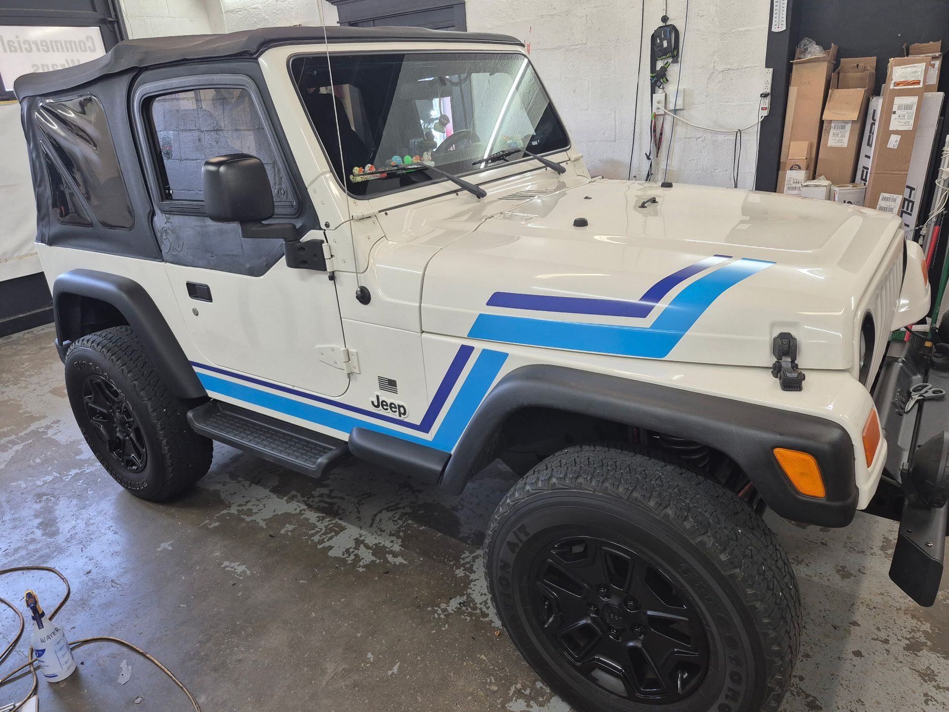 A white jeep with blue stripes on the side is parked in a garage.
