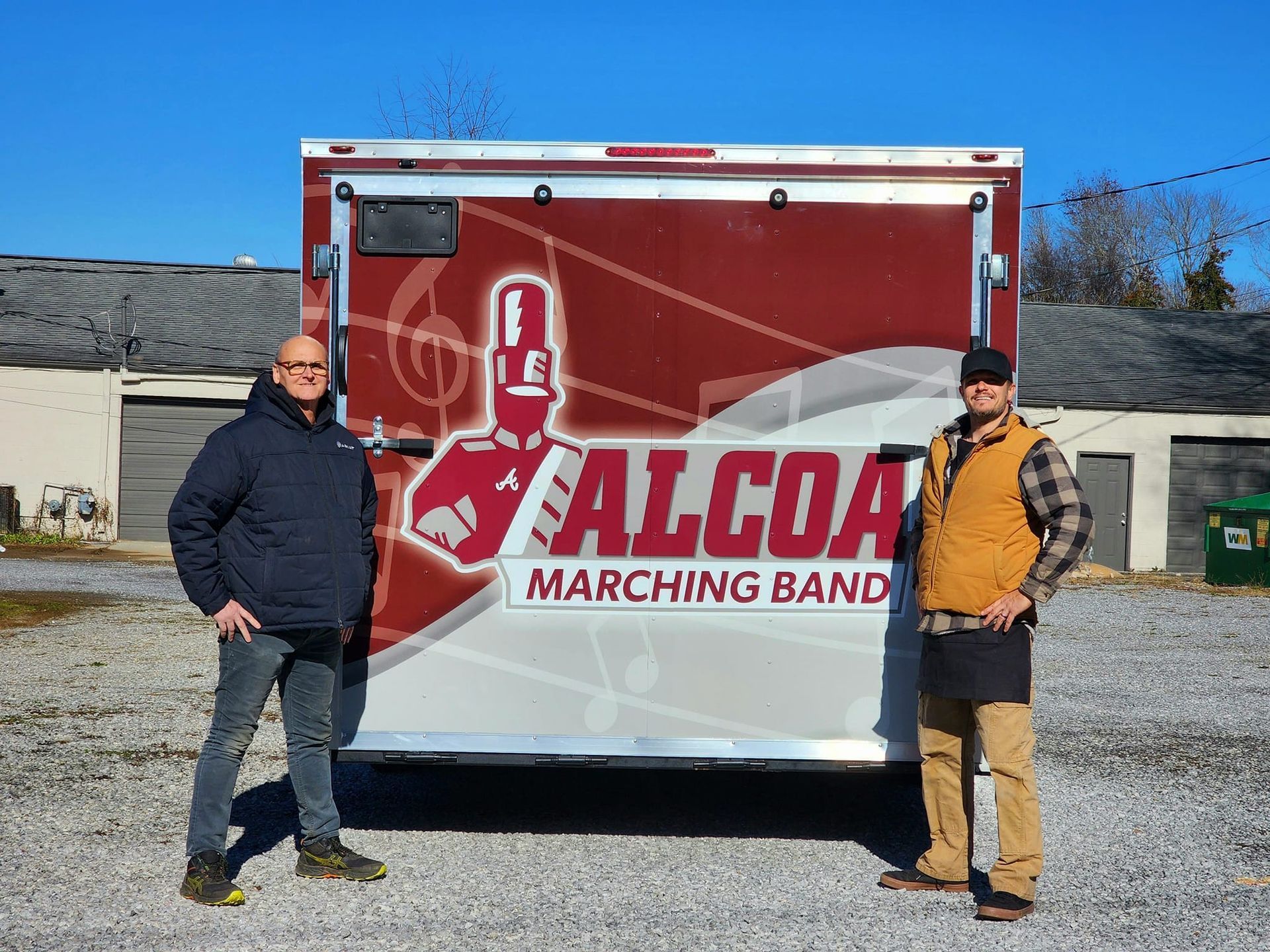 Two men are standing in front of a marching band trailer.