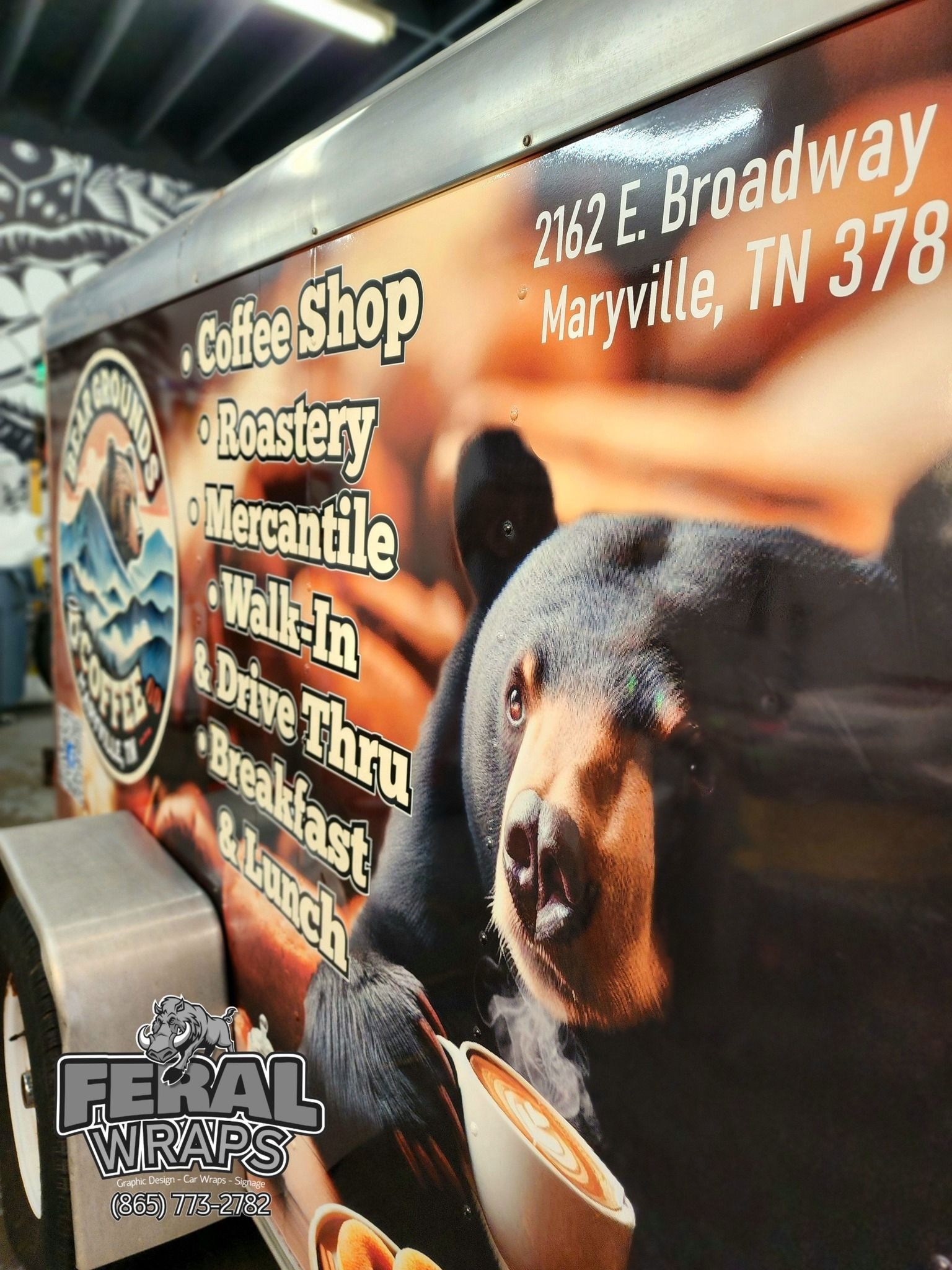 A bear is holding a cup of coffee on the side of a coffee shop trailer.