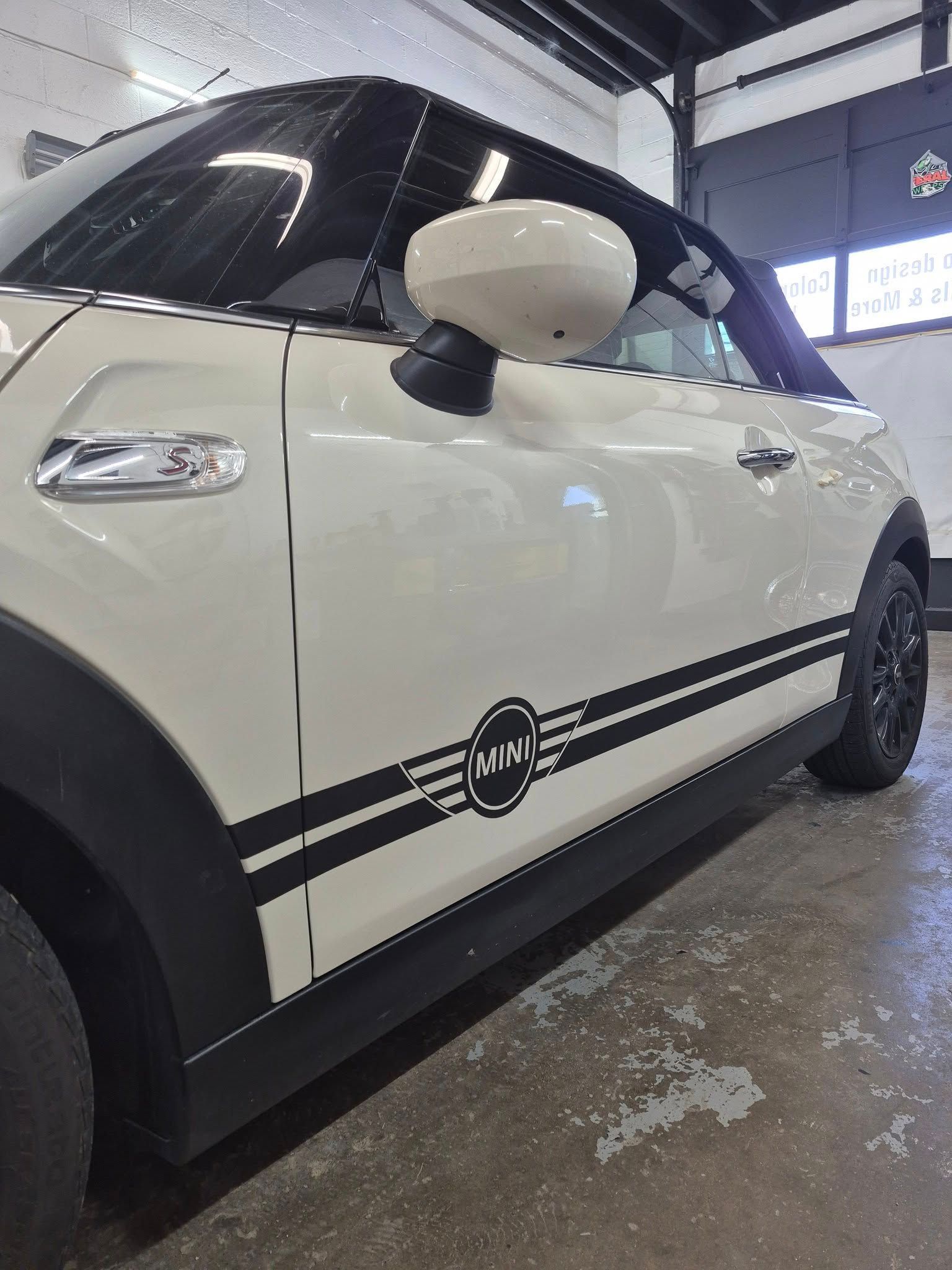 A white mini cooper with black stripes on the side is parked in a garage.