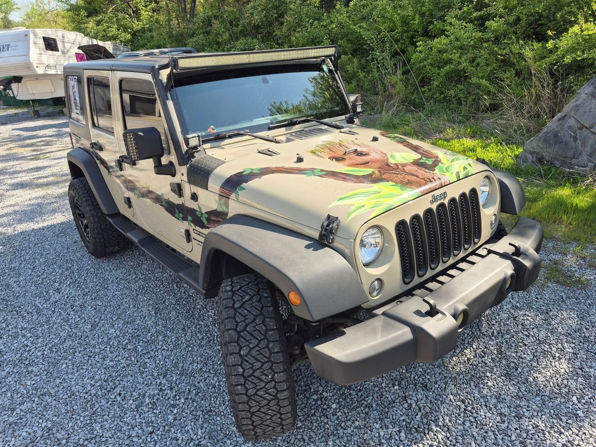 A jeep with a camouflage paint job is parked in a gravel lot.