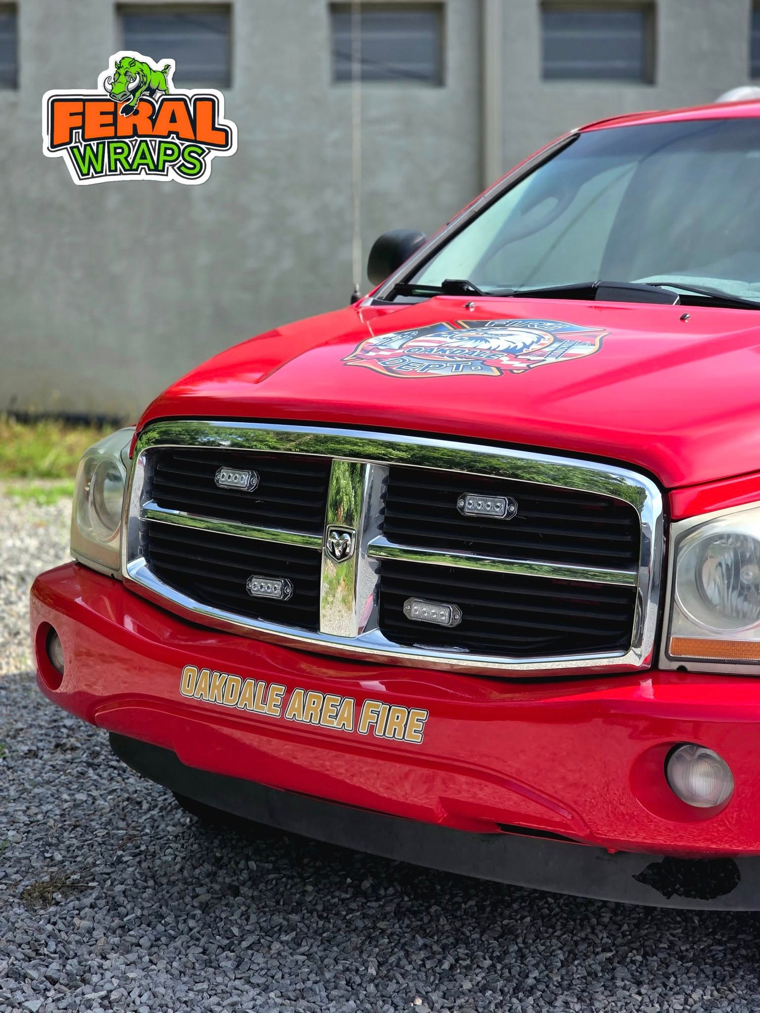 A red dodge ram truck is parked on gravel in front of a building
