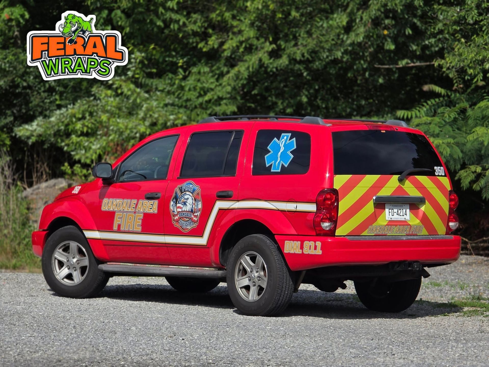 A red ambulance with a yellow stripe on the back is parked on a gravel road.