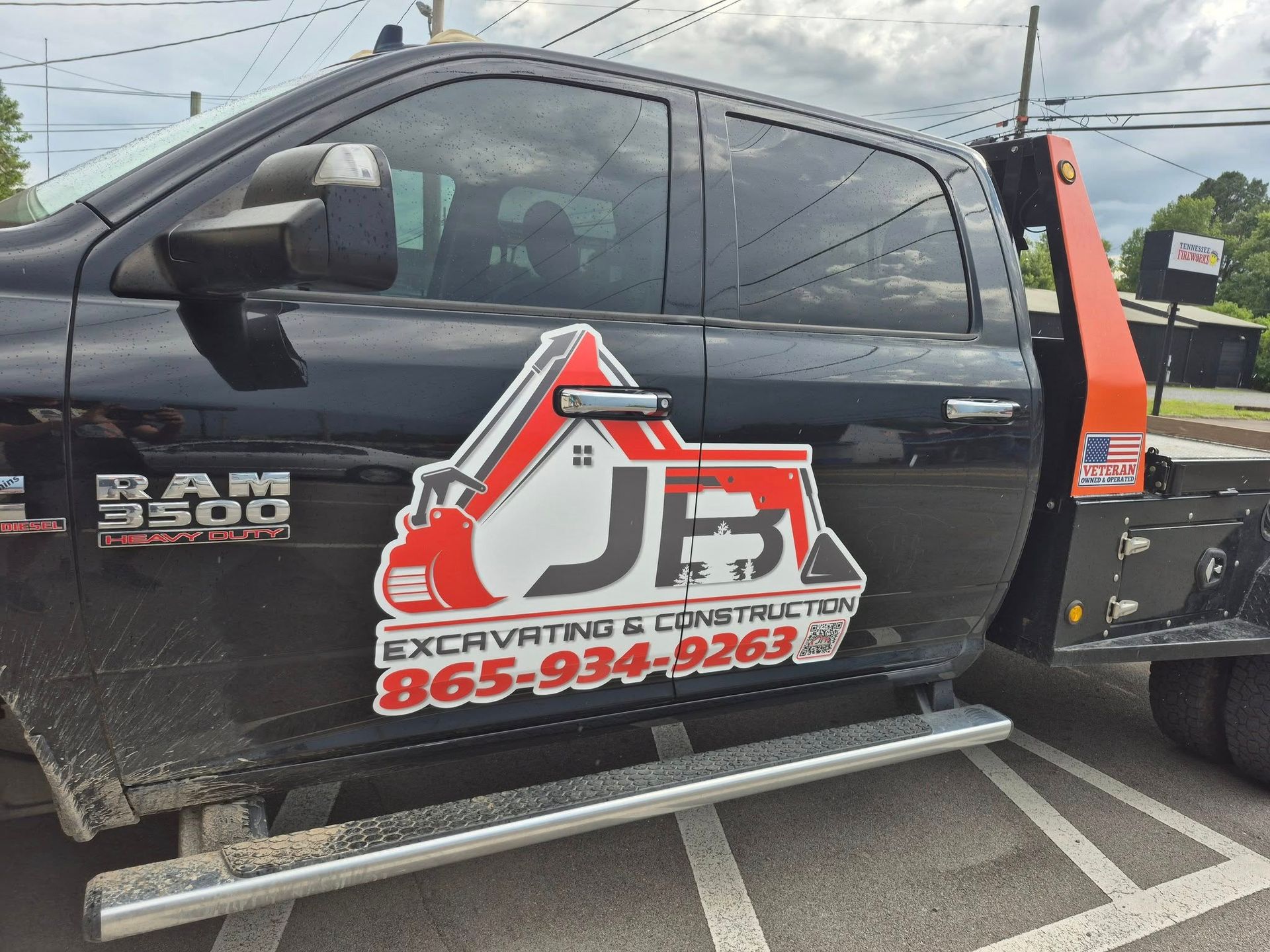 Black RAM 3500 truck with JB Excavating & Construction logo and phone number, parked outdoors.