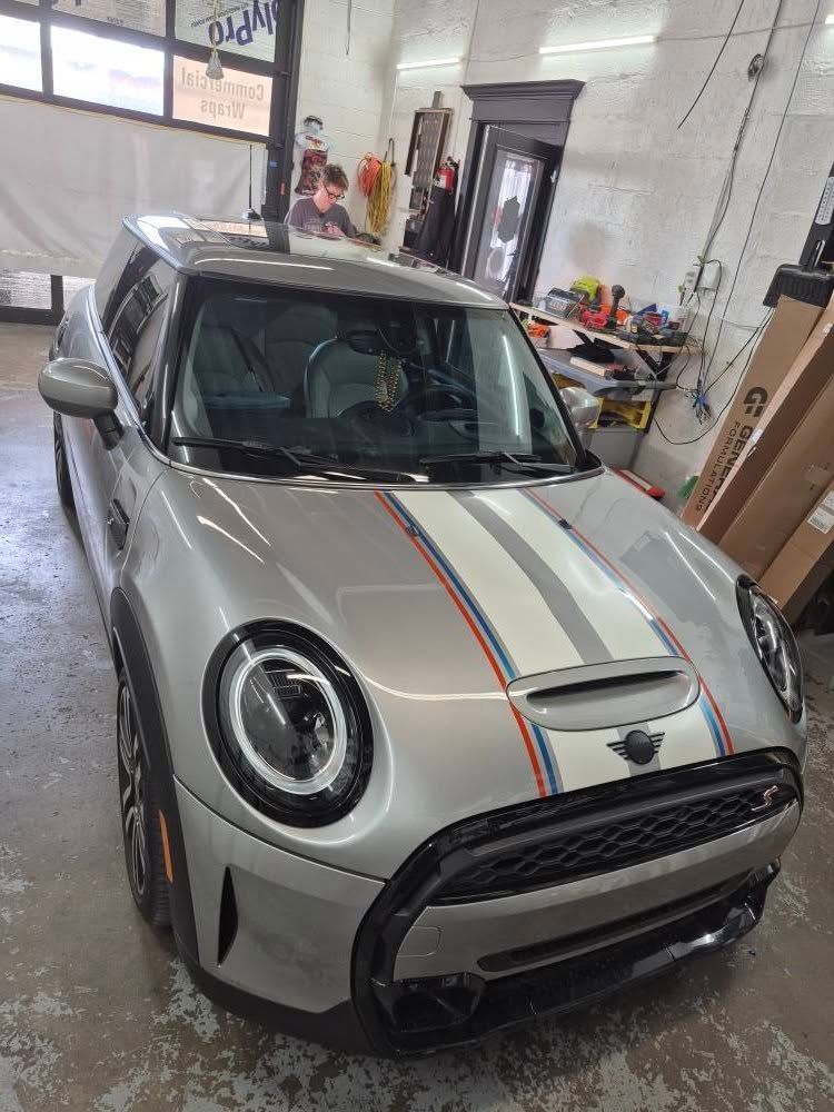 Silver Mini Cooper with racing stripes in a garage.