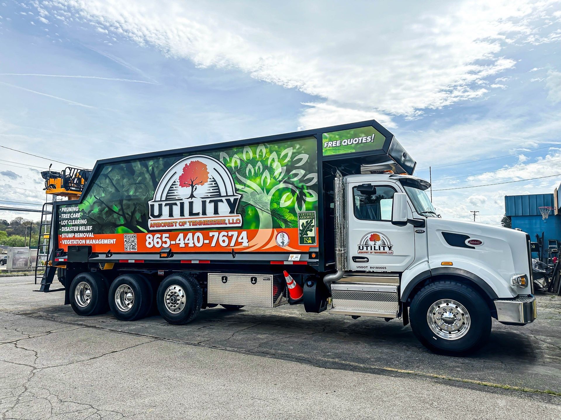 Utility truck with tree-themed graphics and contact info parked outdoors under a cloudy sky.