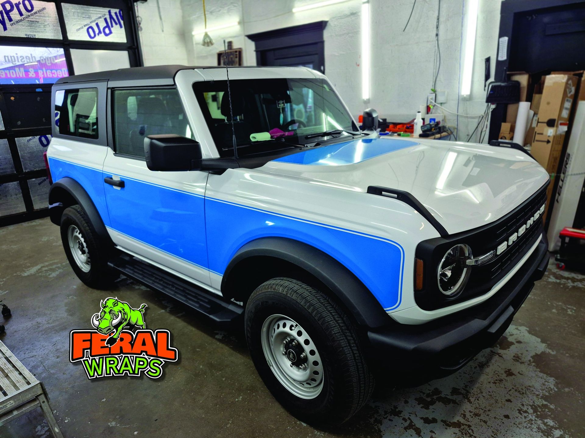 White and blue Ford Bronco with black accents inside a garage.