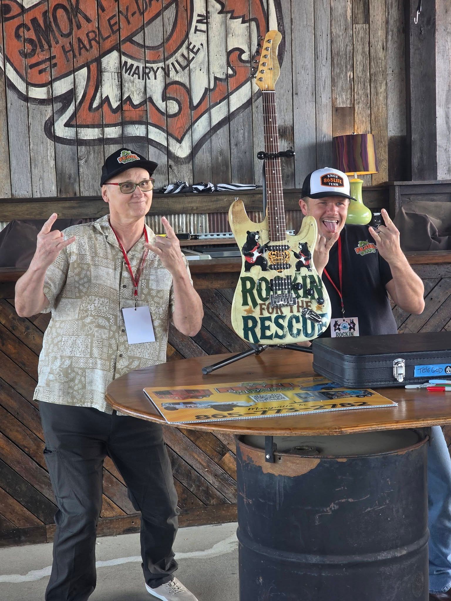 Two people posing behind a table with a “Mushroom Rescue” sign in a rustic indoor setting.