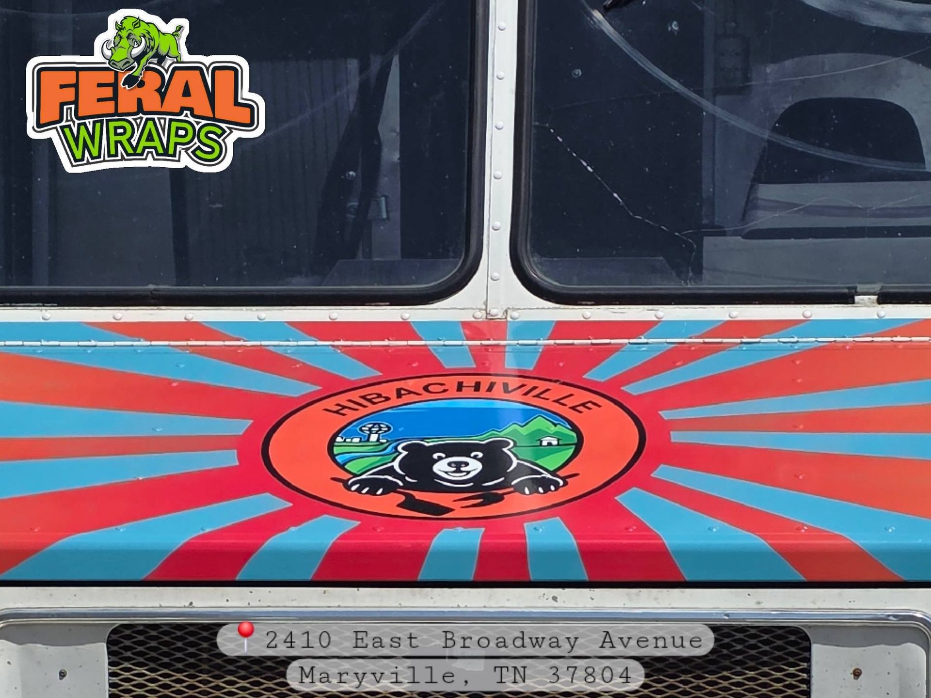 Colorful bus wrap with red and blue sunburst, Feral Wraps logo, and cartoon raccoon emblem on the side.