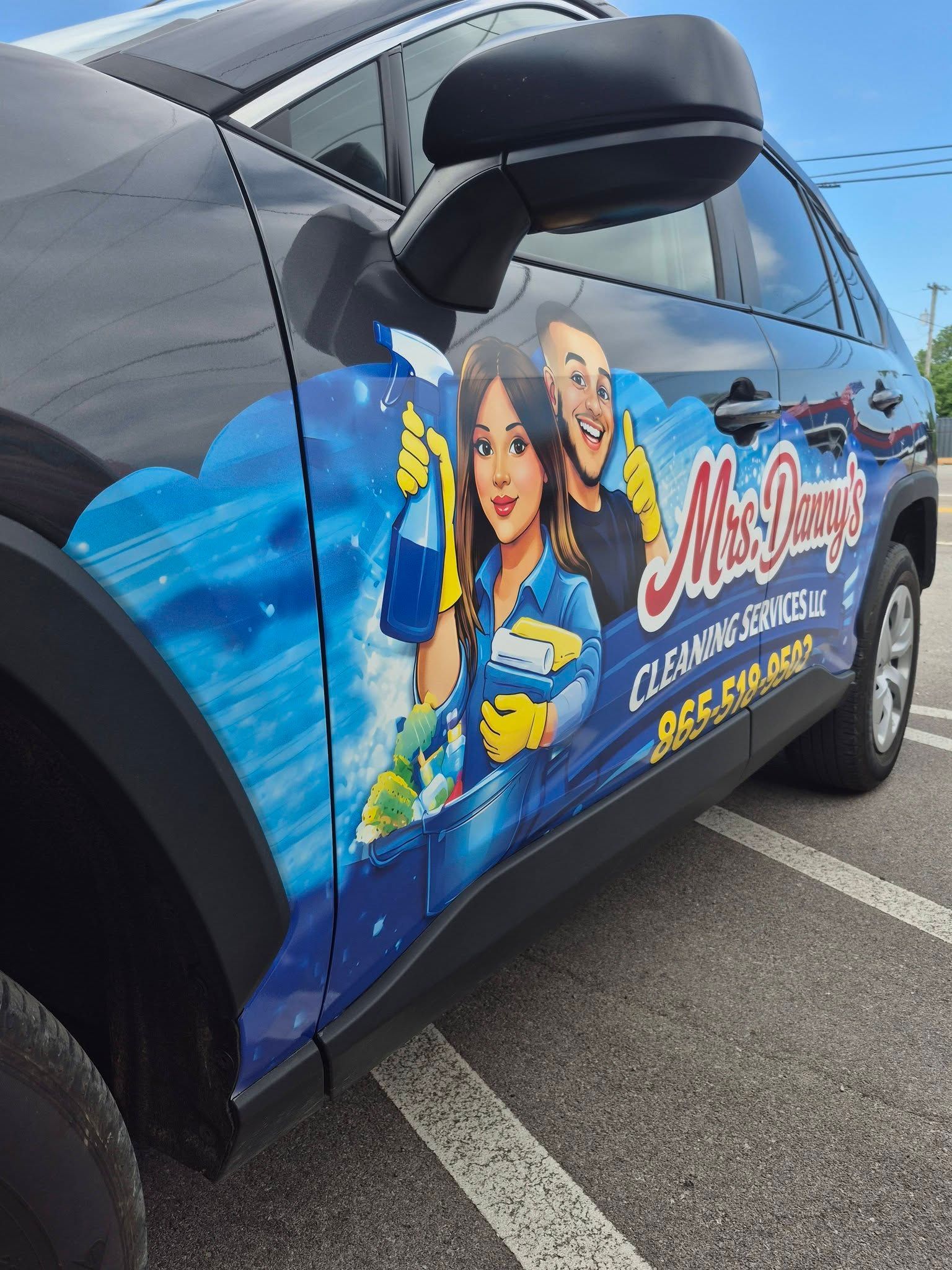 Colorful wrapped car with comic-style superheroes and “Maid” logo parked in a lot