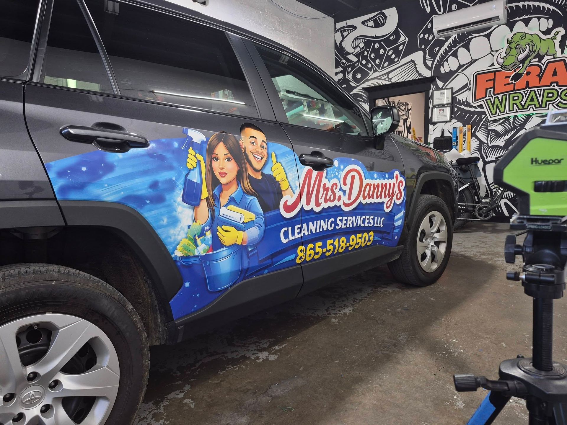 Branded cleaning service van with colorful Miss Daisy’s graphics parked indoors near a camera rig