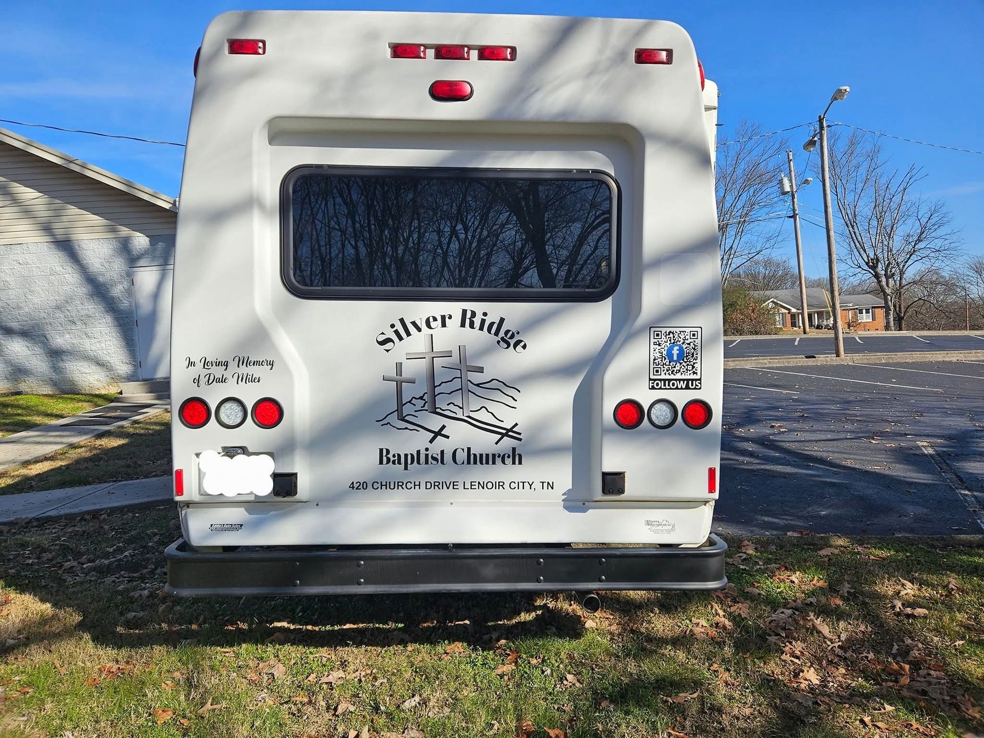 Rear view of a white Silver Ridge Baptist Church bus with logo and lights, parked on grass.