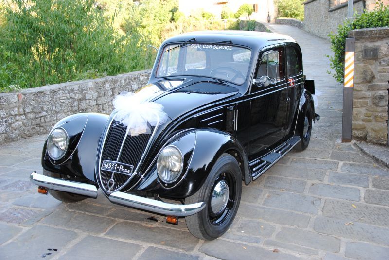 Auto d'epoca nera con decorazioni a nastro bianco parcheggiata su un vialetto di pietra all'aperto
