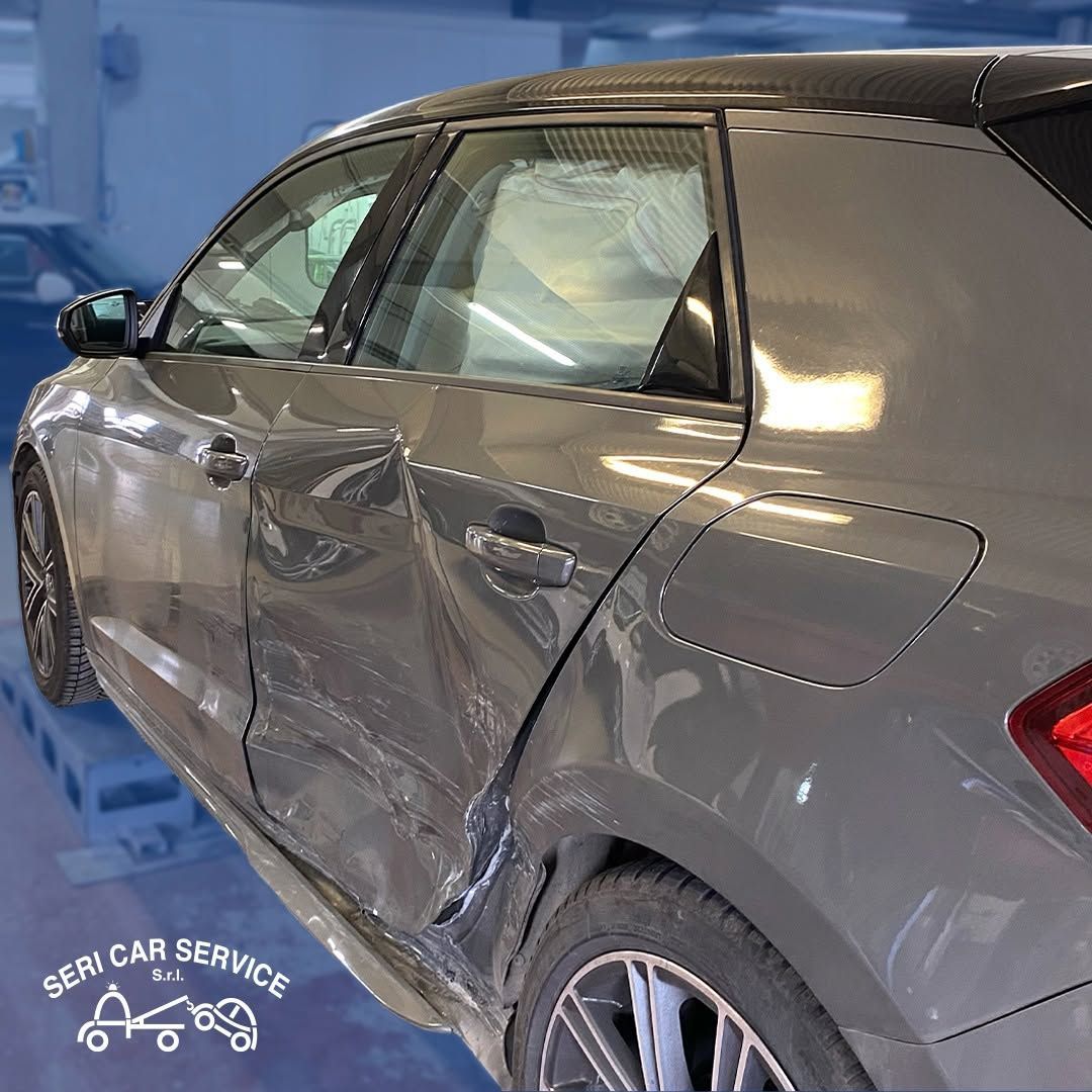 Berlina grigia danneggiata con portellone posteriore accartocciato in un garage coperto.