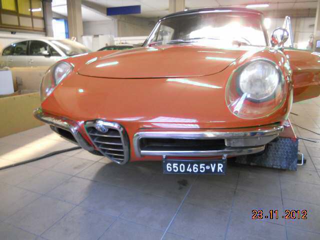 Vista frontale di un'auto d'epoca arancione in un garage, con fari rotondi e targa 650465-VR.