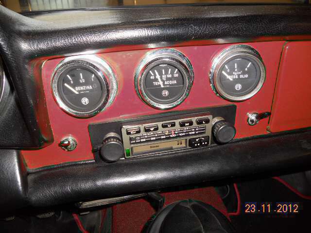 Cruscotto di un'auto d'epoca con tre indicatori e una radio vintage su un pannello rosso.