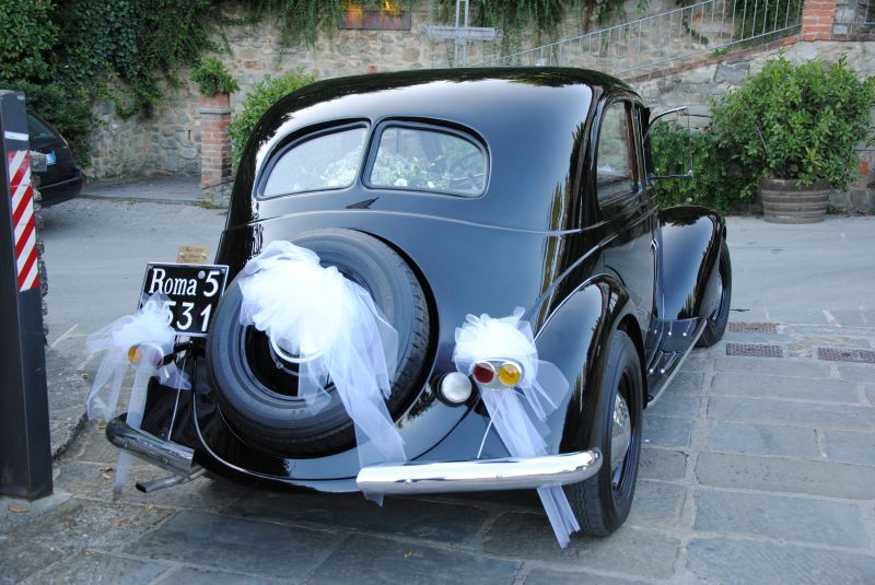 Auto d'epoca nera con decorazioni a nastro bianco parcheggiata su una strada lastricata.