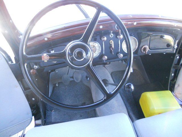 Interni di un'auto d'epoca con volante nero, cruscotto in legno e sedili azzurri.