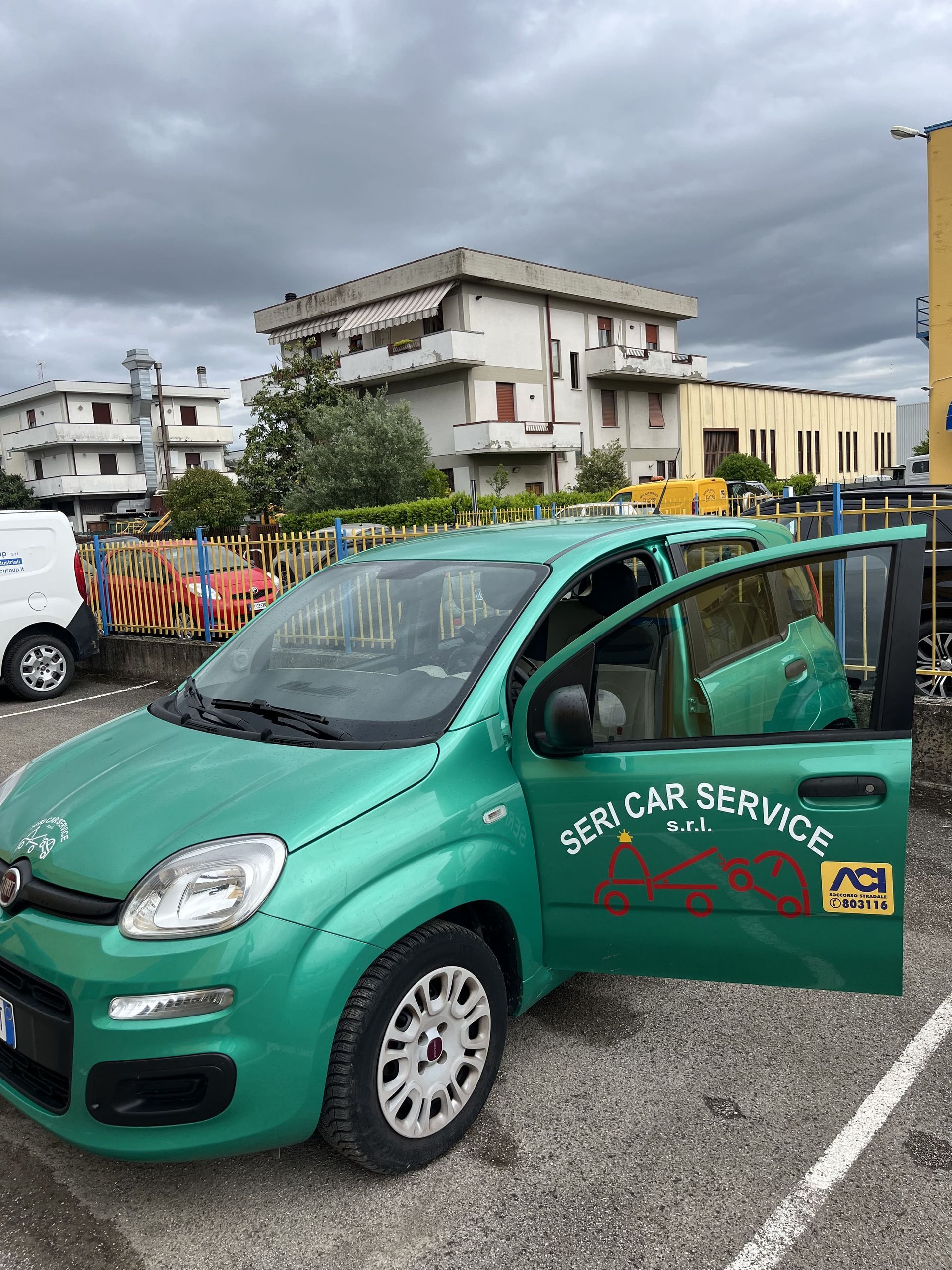 Auto di servizio compatta verde parcheggiata all'aperto con la portiera del conducente aperta in una giornata nuvolosa.