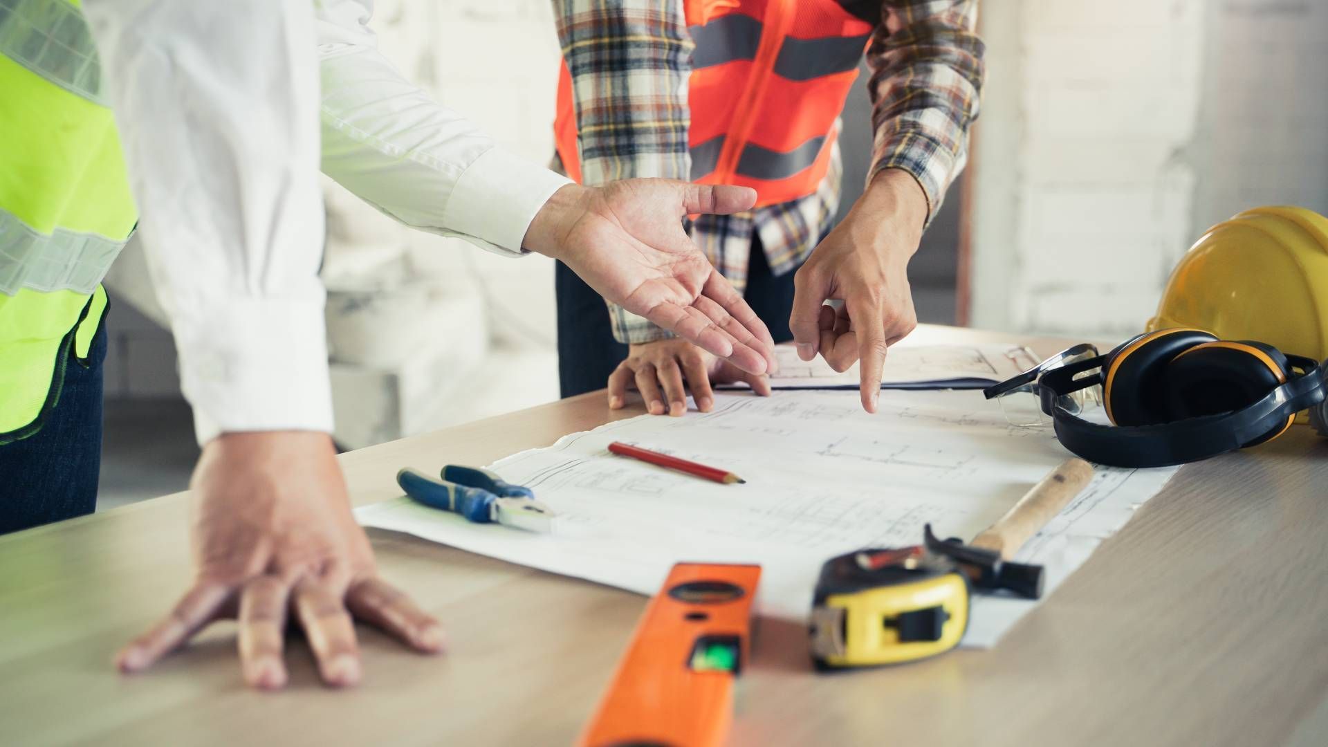 Construction workers reviewing blueprints on a table, tools and safety equipment nearby.