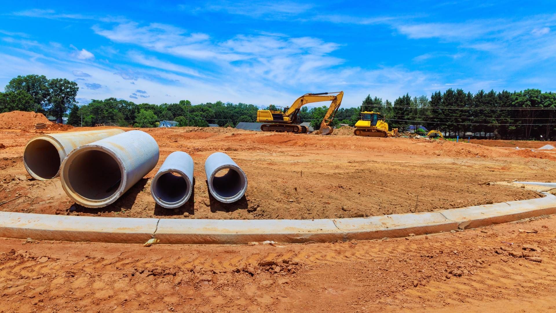 Construction site with concrete pipes, yellow excavator, and bulldozer under a blue sky.
