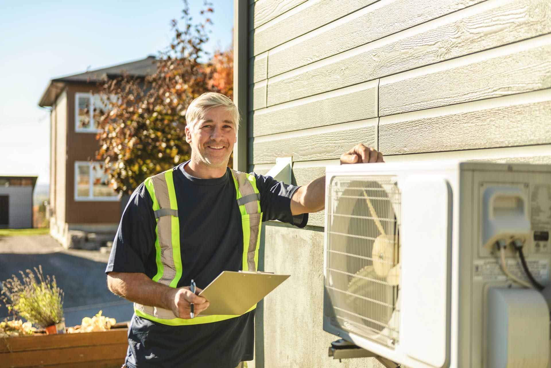 Smiling HVAC technician in a safety vest holding a clipboard beside an outdoor AC unit Smiling HVAC technician in a safety vest holding a clipboard beside an outdoor AC unit