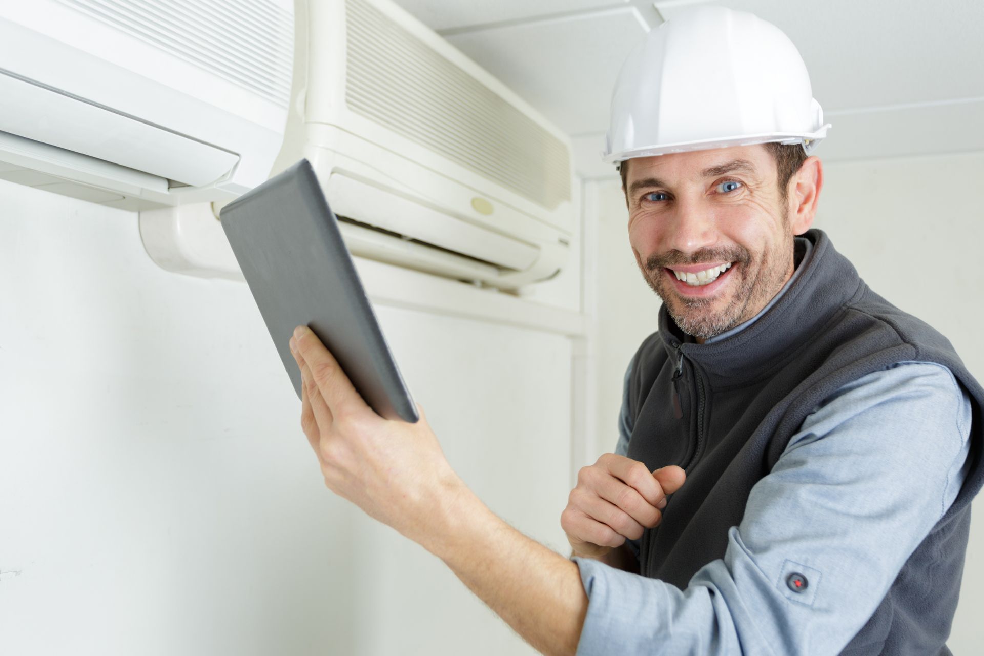 A technician with a tablet by an air conditioning unit.