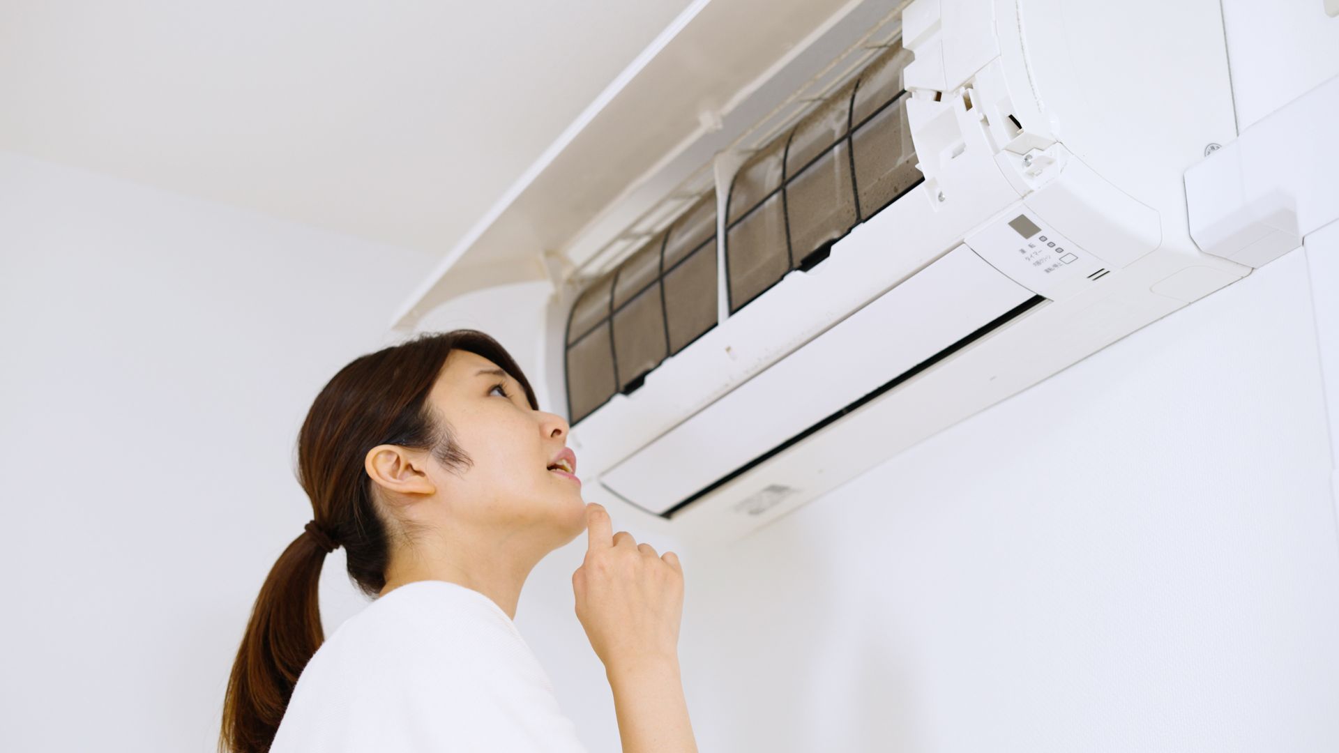 A woman examines an air conditioner, contemplating if it is working or not.