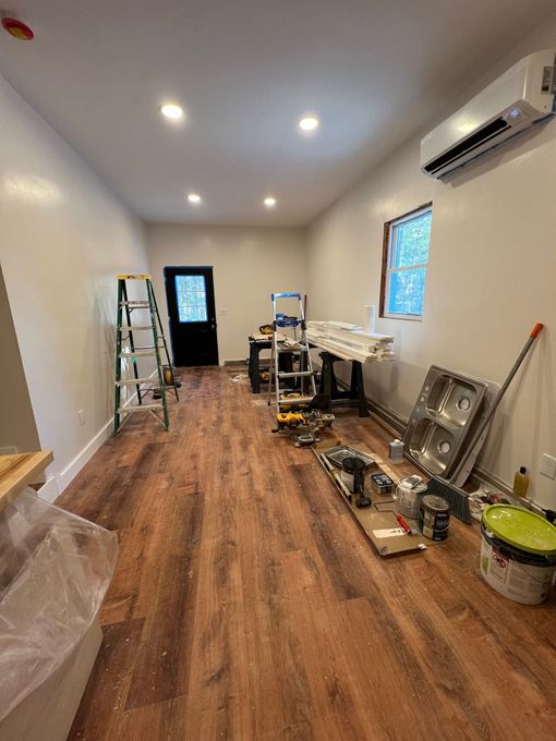 Long narrow room under renovation with ladders, tools, and floor coverings on a wood floor.