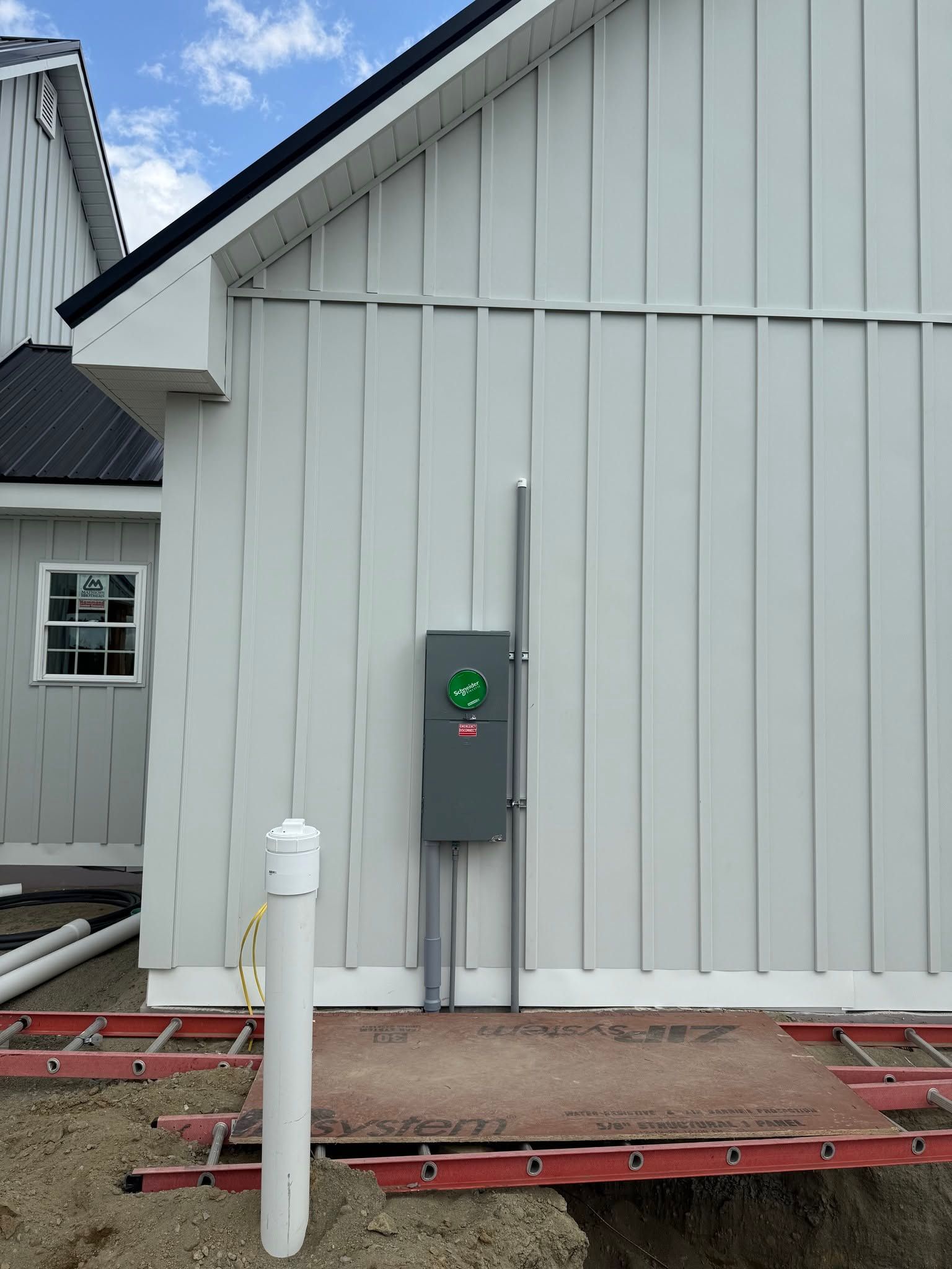 White house exterior with a gray electrical box, conduit, and a white pipe beside a red work platform.