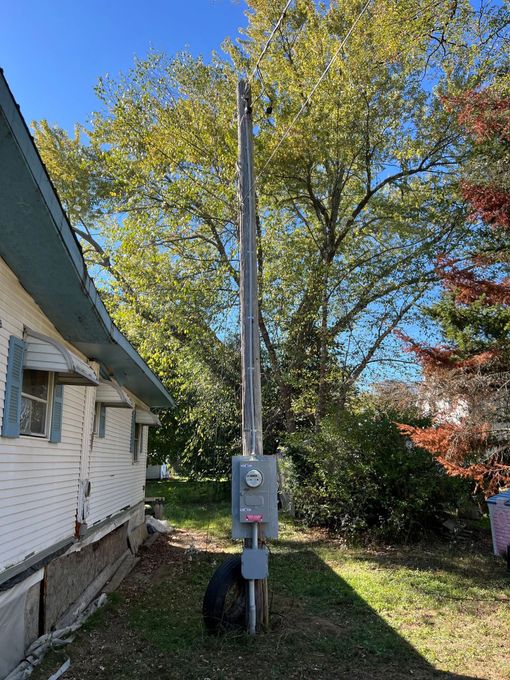 Power pole with utility meter beside a white house, under blue sky and autumn trees