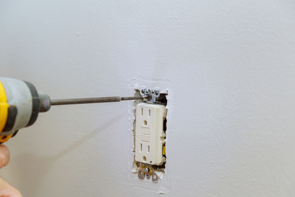 Hand drill removing an electrical wall switch from a white wall