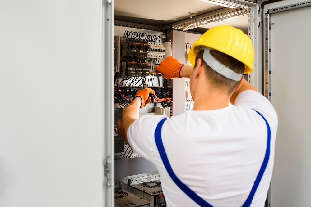 Electrician in yellow hard hat working inside an open electrical panel cabinet