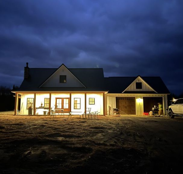 Lit house and garage at dusk under a dark cloudy sky, with a parked vehicle on the right.