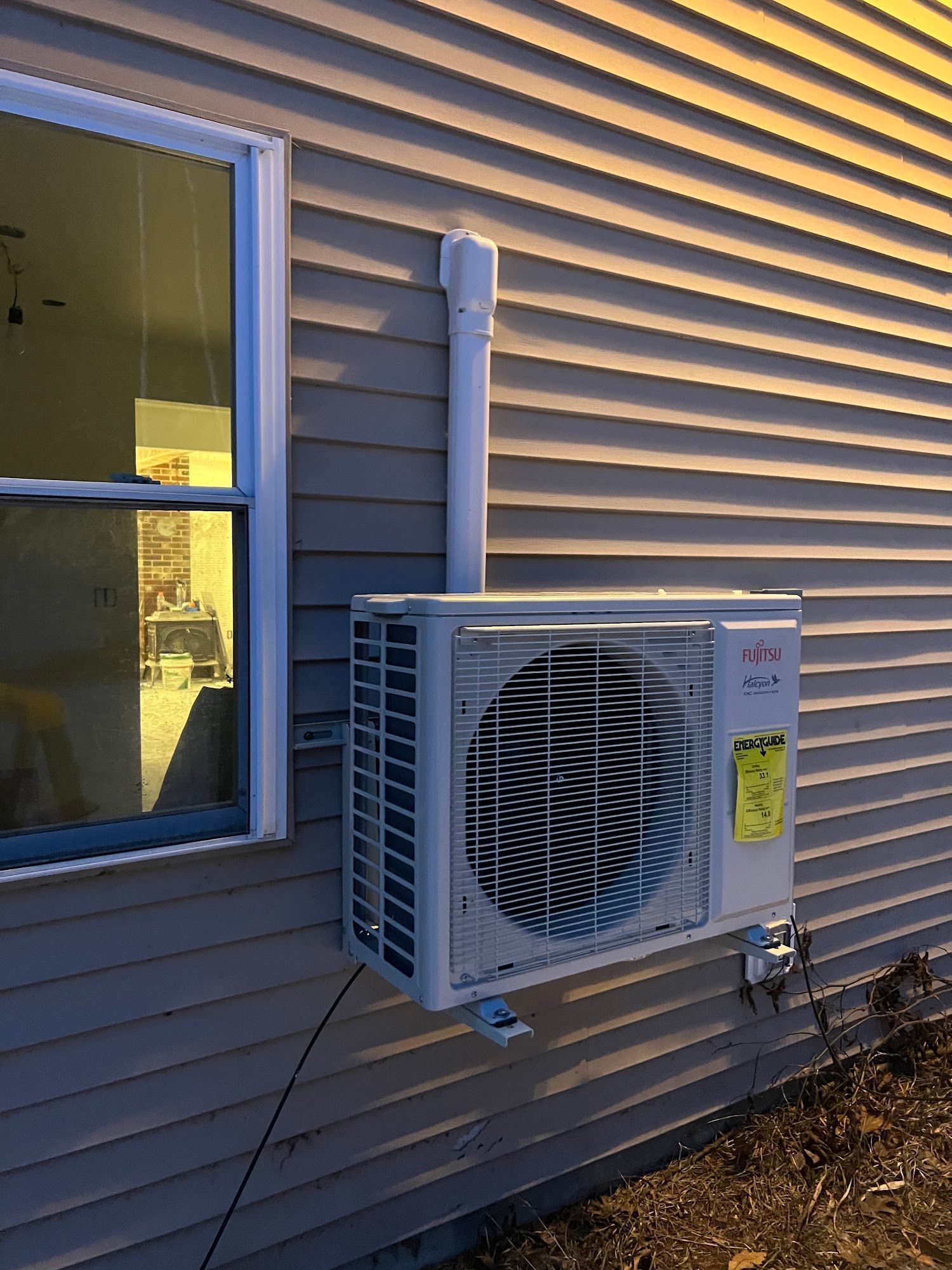 Outdoor wall-mounted air conditioner unit beside a house window with beige siding.