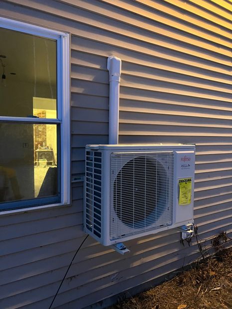 Outdoor air conditioner unit mounted on tan house siding beside a window