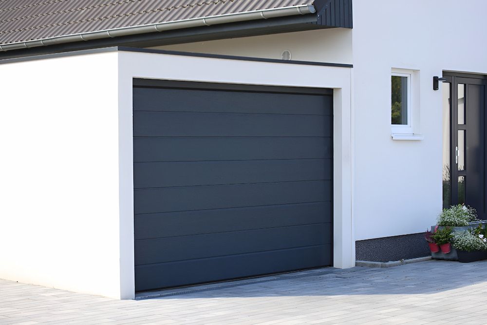 A Black Garage Door Is Sitting In Front Of A White House — Brunswick Valley Door Centre in Main Arm, NSW
