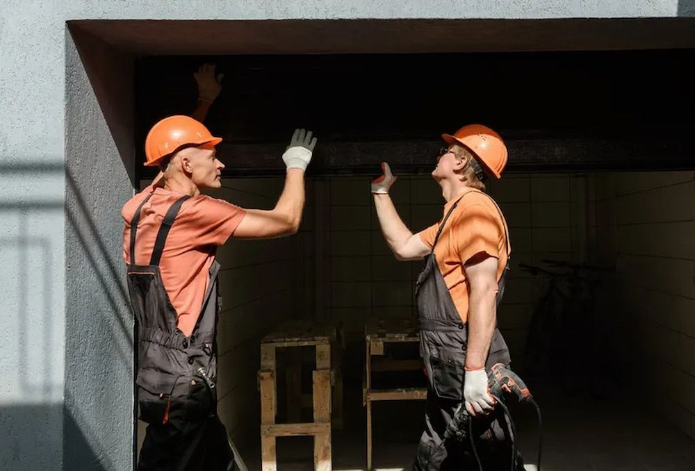 Two Construction Workers Are Working On A Garage Door — Brunswick Valley Door Centre in Northern Rivers, NSW