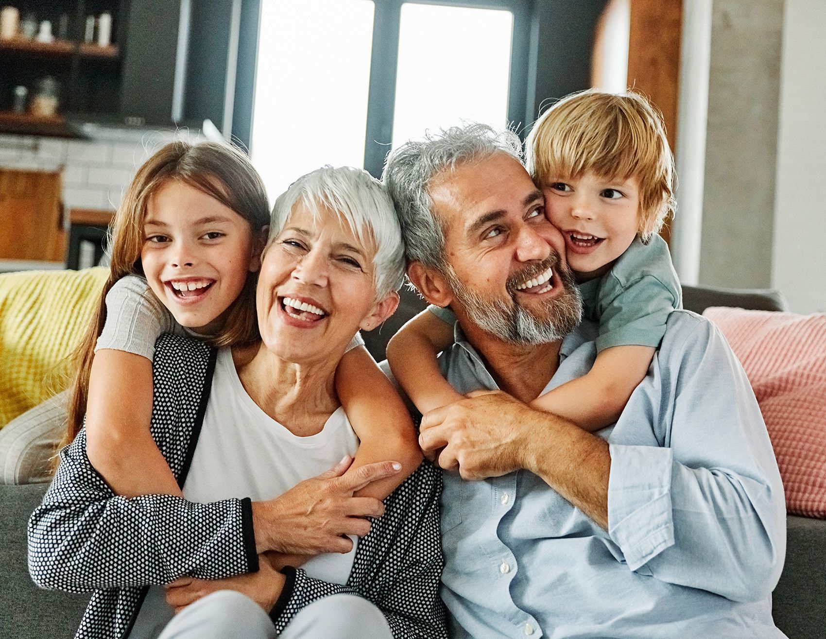 Smiling family sitting on a couch, hugging in a cozy living room with large windows.