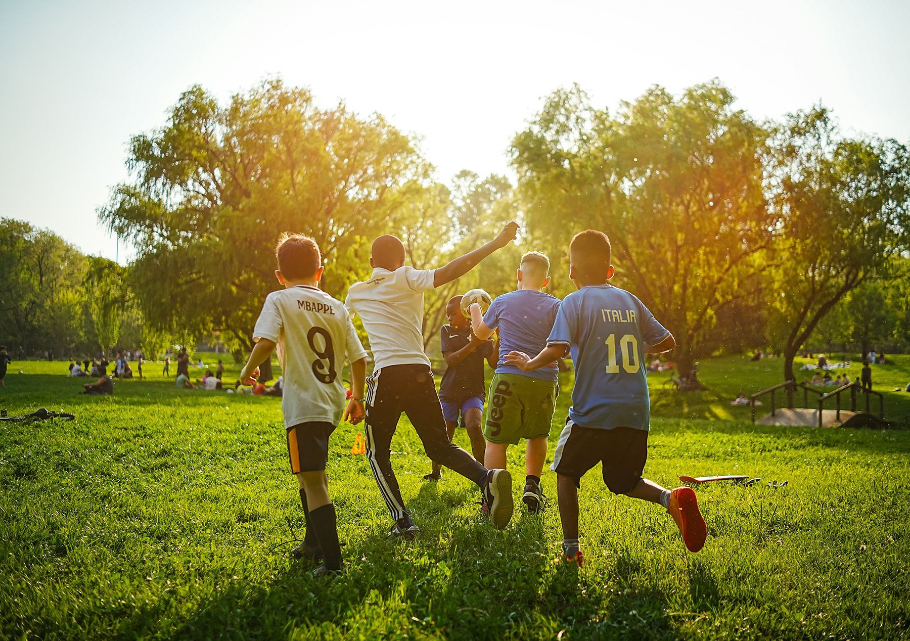 Friends playing soccer in a sunny park with trees and green grass