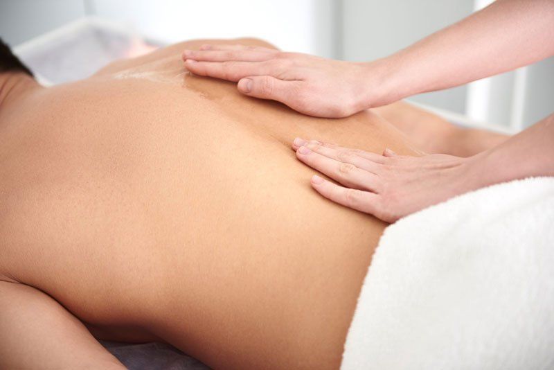 A person lying on a massage table while receiving a back massage with gentle pressure from a therapist's hands.
