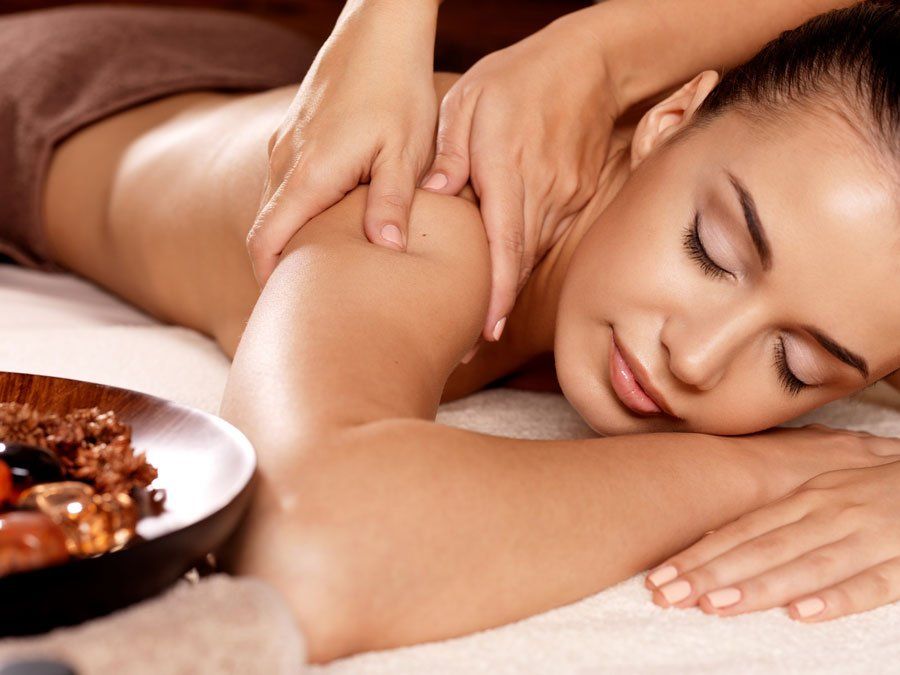 Woman receiving shoulder massage, lying face down on massage table with bowl of items next to her.