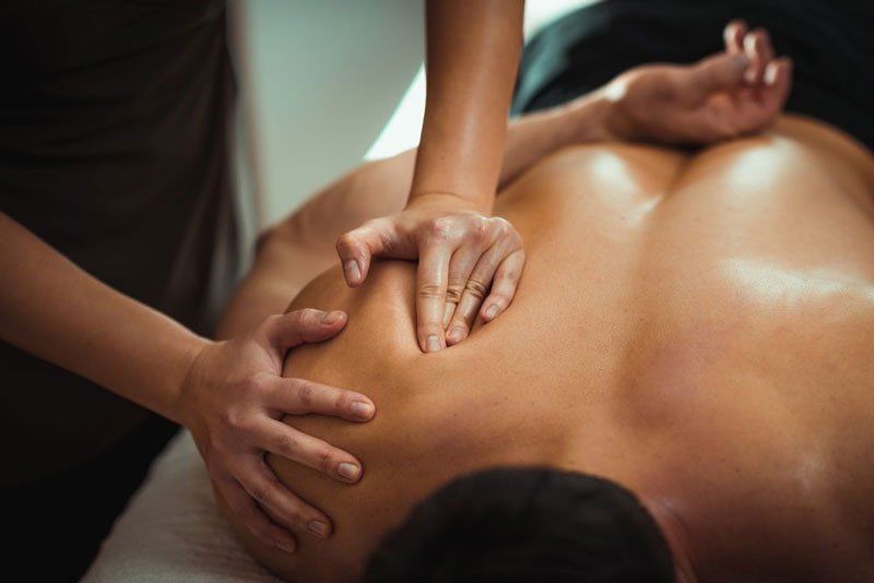 A therapist performing a deep tissue massage on a person's shoulder while they lie on a massage table.