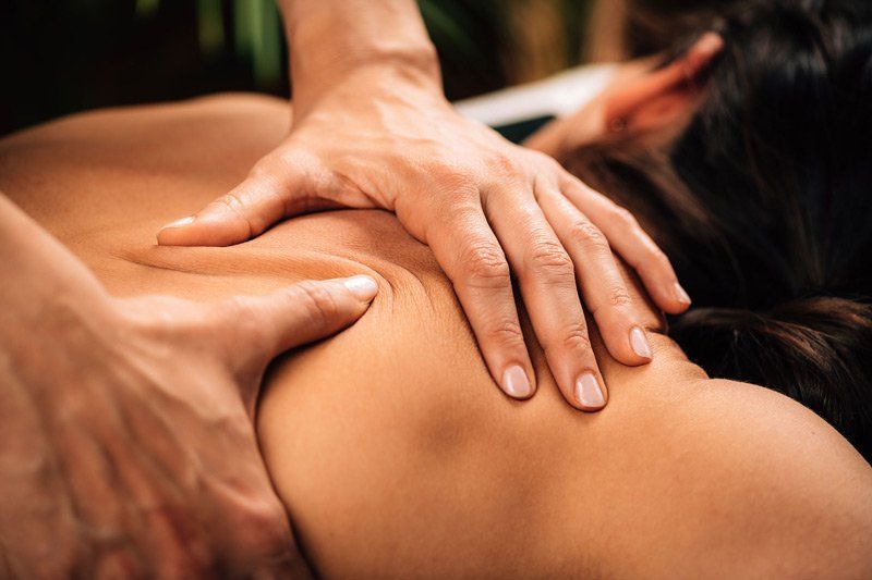 Hands massaging a person's upper back and shoulder.