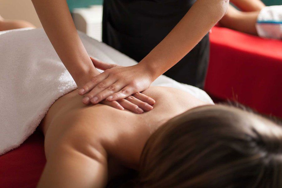 A massage therapist performing a back massage on a person lying on a red treatment table.